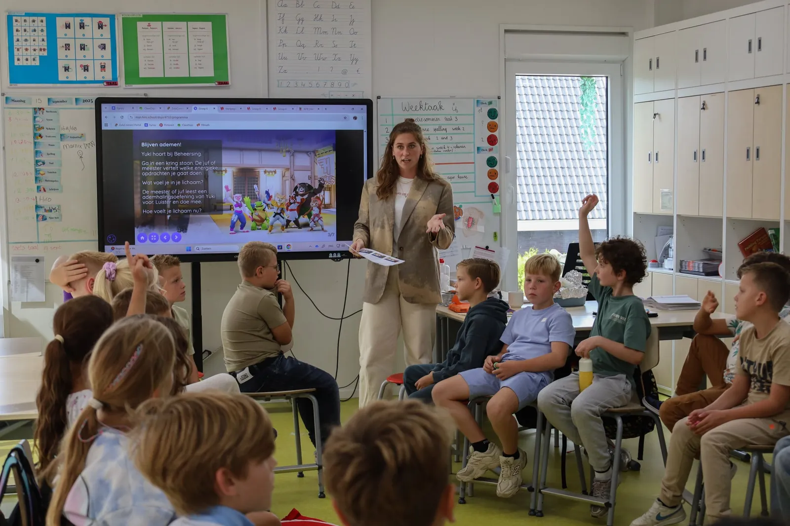Leerkracht geeft een les van HiRO voor de groep, kinderen steken hun vinger op