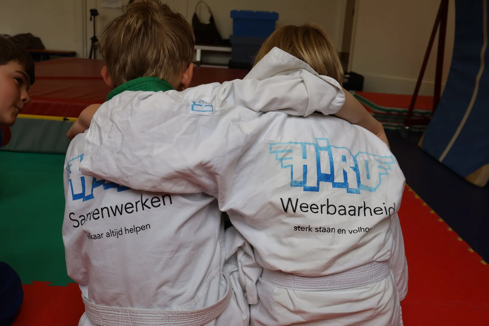 Twee kinderen in judopak met een arm om elkaars schouder
