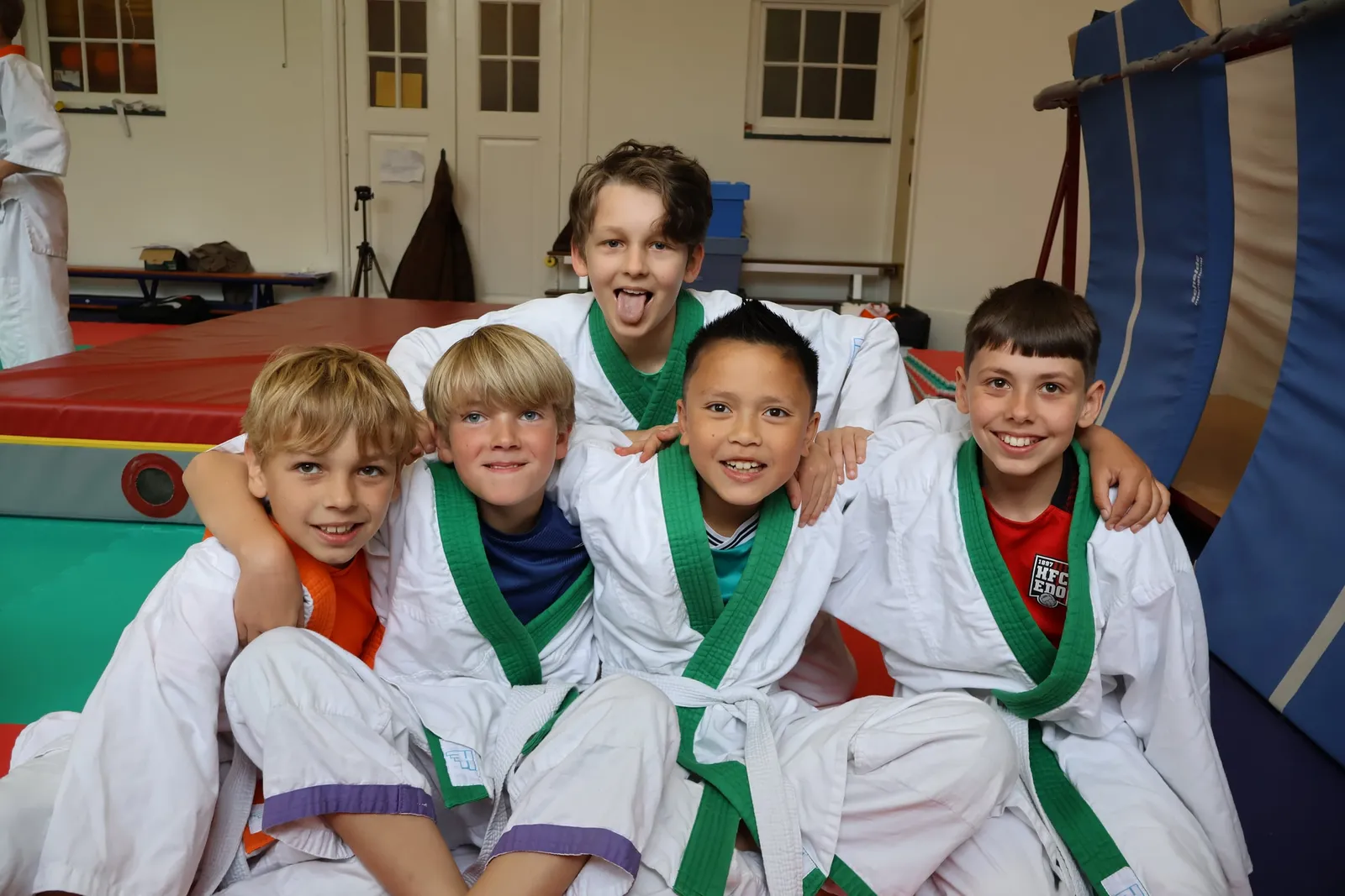 Een groep lachende kinderen in judopak op de mat
