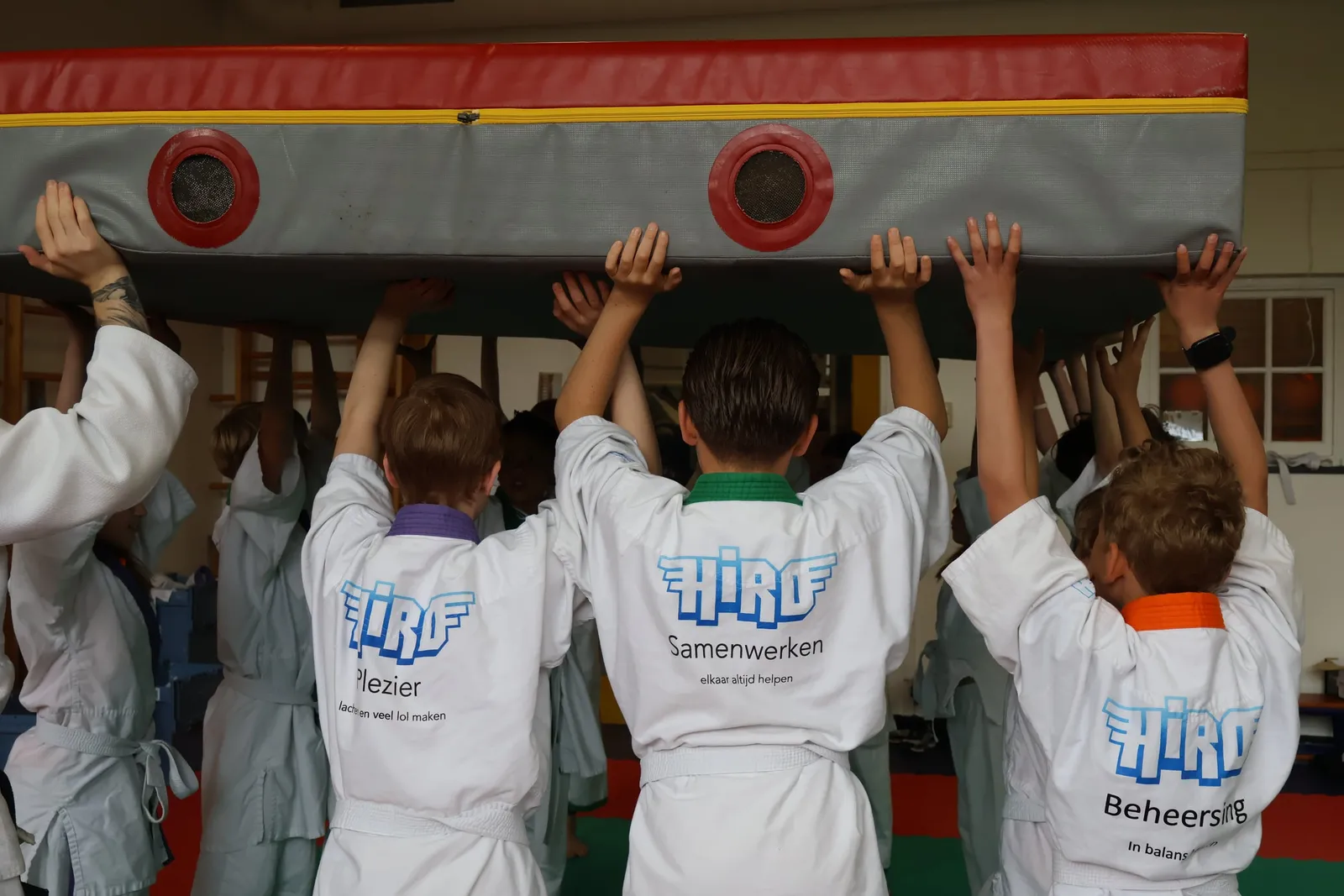 Kinderen in judopakken tillen samen een grote mat op tijdens Schooljudo